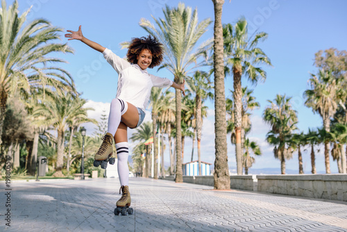 Εκτύπωση καμβά Black woman on roller skates rollerblading in beach promenade with palm trees