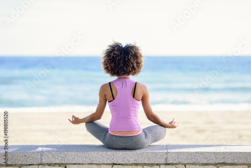 Black woman, afro hairstyle, doing yoga in the beach