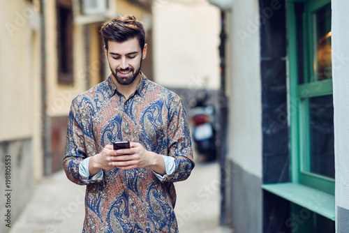 Young man wearing casual clothes looking at his smartphone in the street.