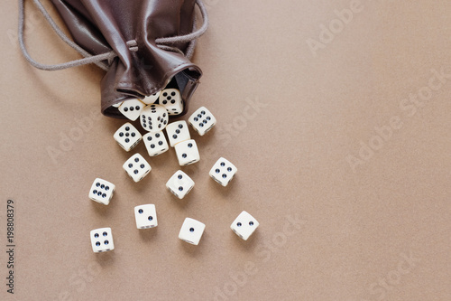 Set of white gaming dice rolled out of leather bag on brown background. Concept with copy space for games, game board, role playing game, risk, chance, good luck or gambling. Toned image top view. 