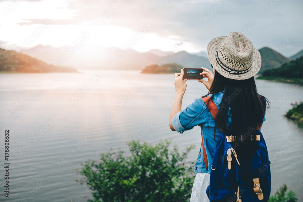 Obraz premium Woman traveler take photo view of lake and mountain with mobile phone.backpacker young girl standing at dam ridge. 