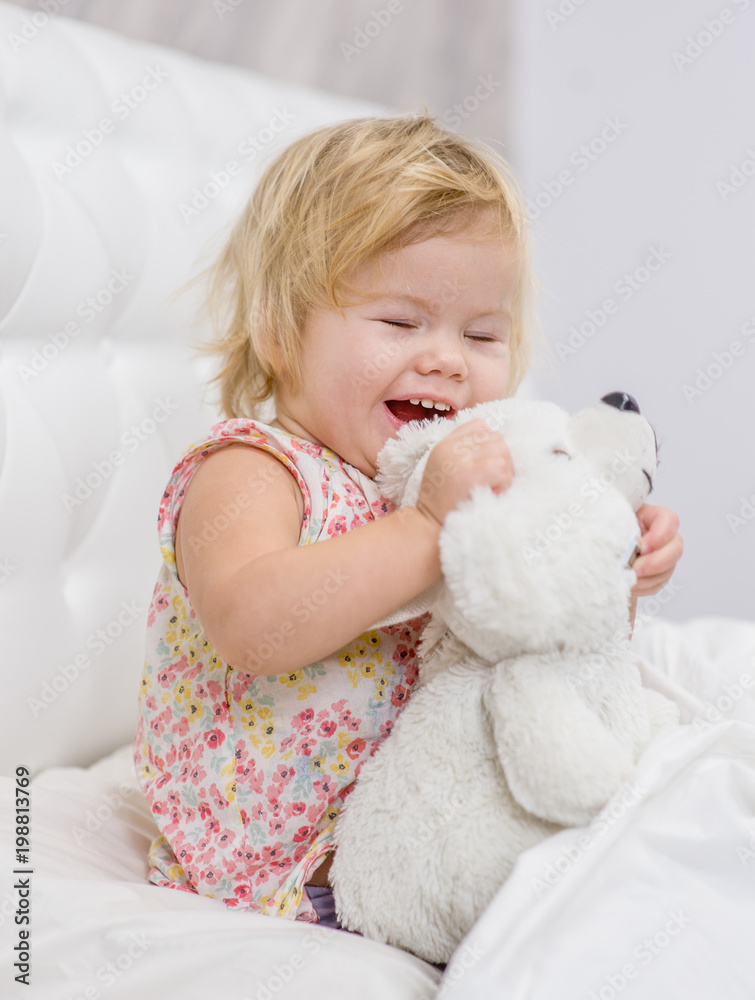 Baby girl playing with toy bear on the bed