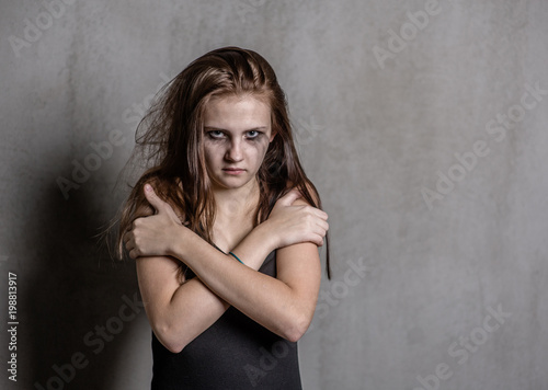 Scared and sad teen girl is clasping his shoulders and looking at camera. Space for text