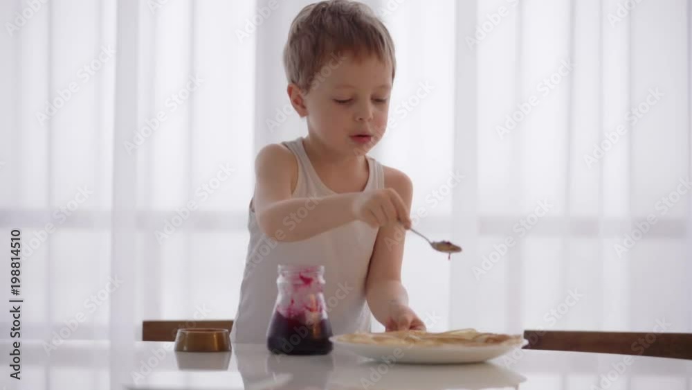 The boy eats the pancakes with jam at white kitchen The boy eats the pancakes with jam at white kitchen
