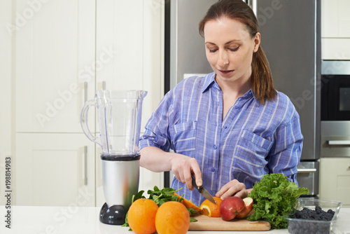 Woman In Kitchen Chopping Fruit To Put Into Juicer