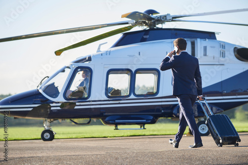 Schilderij op canvas Rear View Of Businessman Walking Towards Helicopter Whilst Talking On Mobile Pho