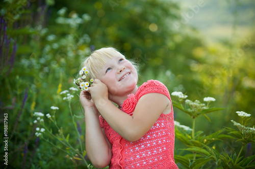 The girl is blonde among the tall flowering herbs in the summer.