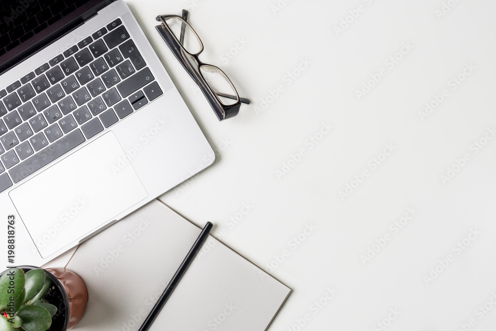Top view of office workplace. White desk with copy space. Flat lay view on table with laptop, glasses, pen, notebook and green flower. Creative designer concept. Top view of office workplace. White desk with copy space. Flat lay view on table with laptop, glasses, pen, notebook and green flower. Creative designer concept.