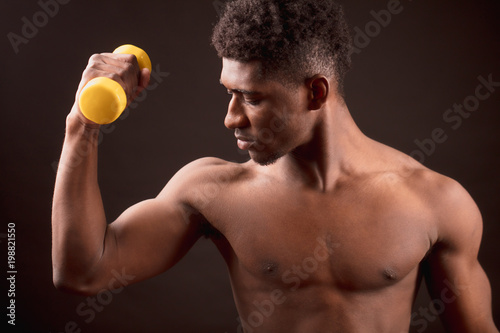 Confident African man training with yellow dumb-bell on the black background. go in for sport photo