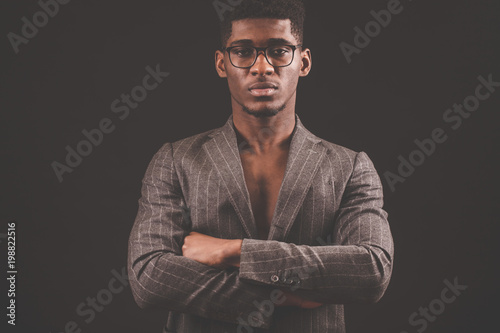 Portrait of successful serious Afro man in glasses with crossed arms isolated on the black background. confident leader © alfa27