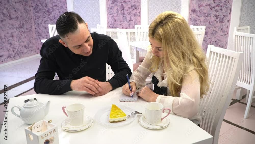 Loving couple in a cafe. Couple man and woman talking in the cute cafes and write in a notebook entry Loving couple in a cafe. Couple man and woman talking in the cute cafes and write in a notebook entry