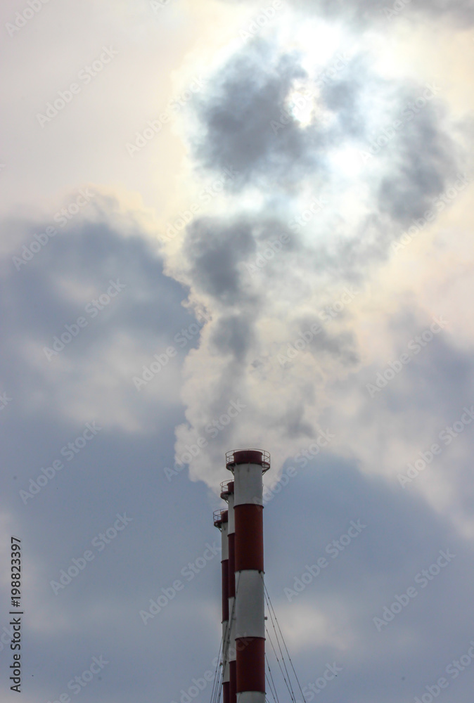 Sunshine struggling through the smoke cloud from three industrial plant chimneys standing in a row against a the cloudy sky Sunshine struggling through the smoke cloud from three industrial plant chimneys standing in a row against a the cloudy sky