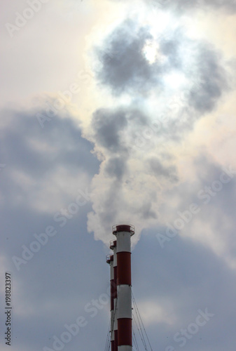 Sunshine struggling through the smoke cloud from three industrial plant chimneys standing in a row against a the cloudy sky 