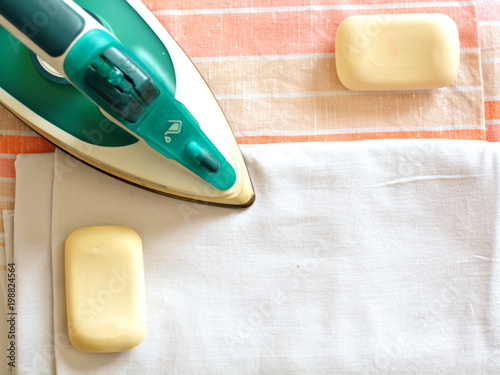 Electric steam iron presser, piece of soap and folded clean washed ironed cotton bed linen in neutral hues. Manual labor