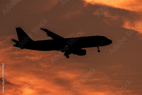 Silhouette passenger airplane flying away in to sky high altitude on sunset