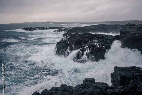 Rugged Icelandic coastline with big waves hitting the black rocks at overcast evening in south west Iceland.