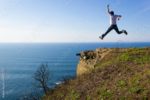 Fearless man jumps high in the air by cliff edge on sunny day. Adventure traveler. Entrepreneur success, no fear, dare concept