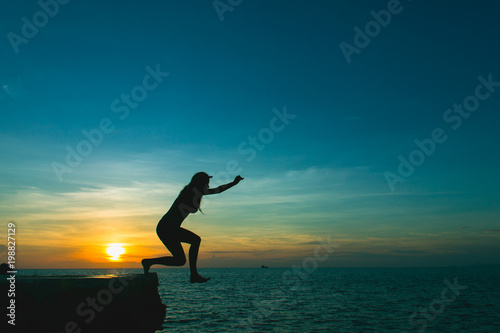 Silhouette of brave girl jumping off cliff to ocean at splendid sunset in the island of Ko Phangan  Thailand. Dare  no fear concept