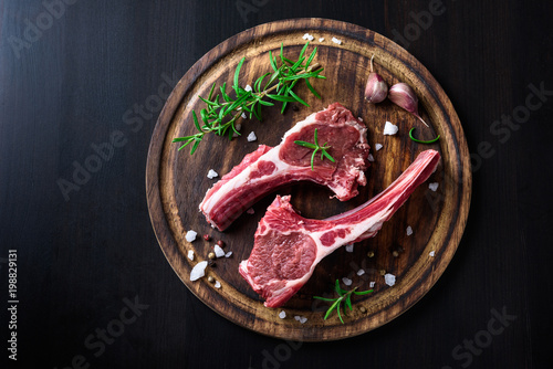 Two raw lamb chops on a wooden cutting board with spices on a dark wooden background