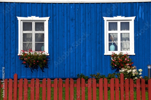  Blue house wall with windows in white frame. rounded off with the red garden fence