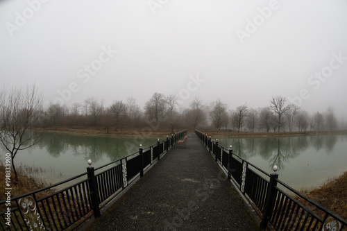 Amazing landscape of bridge reflect on surface water of lake, fog evaporate from pond make romantic scene or Beautiful bridge on lake with trees at fog. © zef art