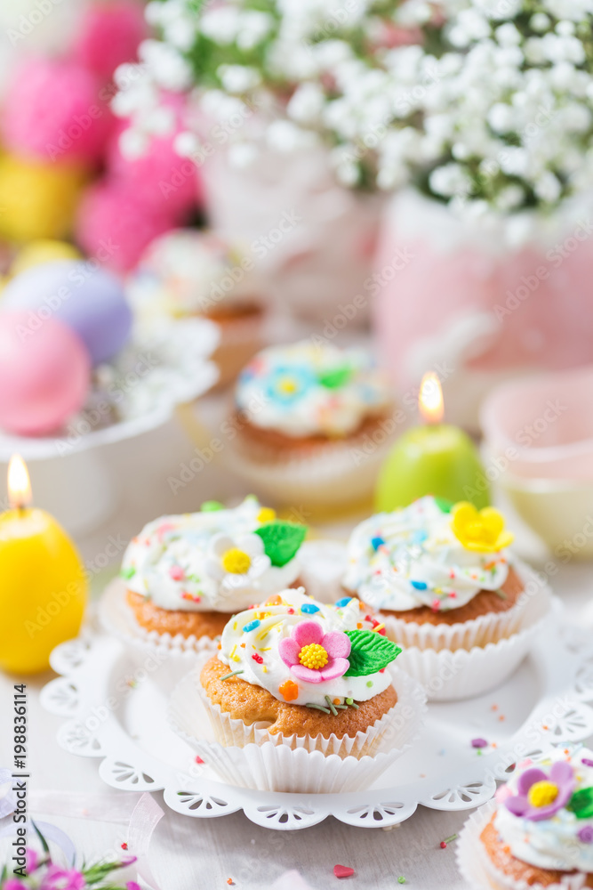 Easter cupcakes with sugar flowers, pastel color eggs and candles on a light background