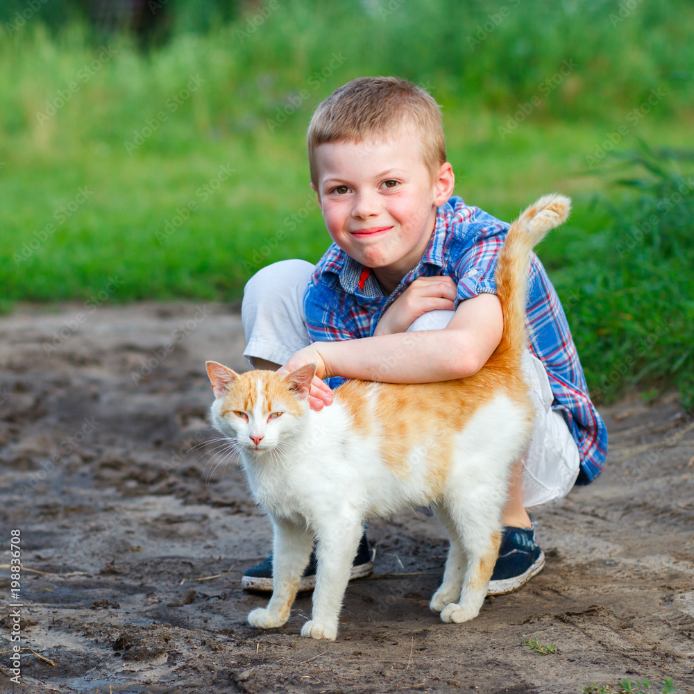 smiling little boy affectionately embraces a red cat. outdoor smiling little boy affectionately embraces a red cat. outdoor