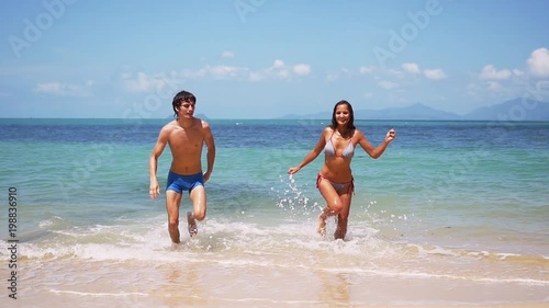 Young happy tan couple running go ut from the tropical sea in slow motion on sunny day. 1920x1080