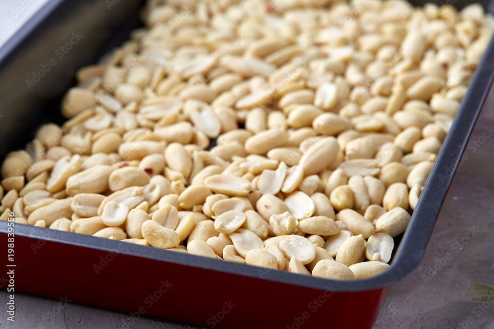 Peeled peanut on baking tray over white textured background, selective focus, shallow depth of field.