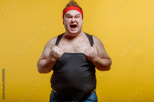 Canvas-taulu Furious fat man wearing red headband and black shirt screams on dark background