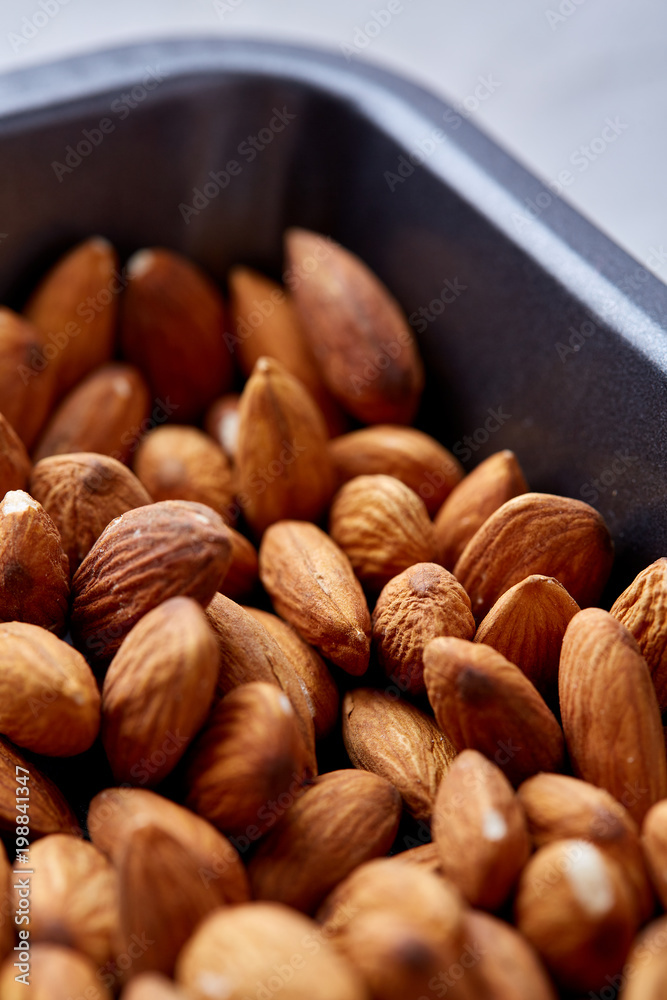 Raw almond on baking tray over white textured background, selective focus, shallow depth of field.