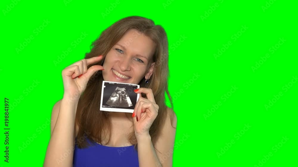 pregnant woman is holding sonogram looking at camera and smiling. pregnant woman is holding sonogram looking at camera and smiling.