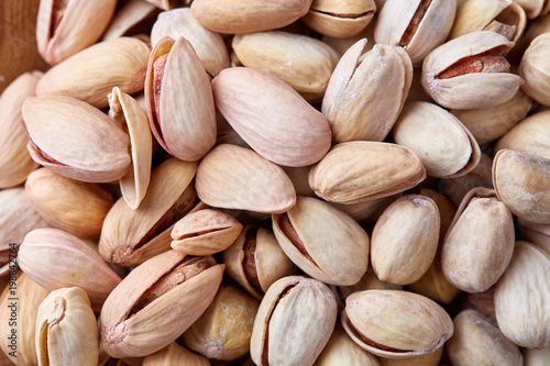 Salted pistachios on a wooden plate over white background, top view, close-up, selective focus.