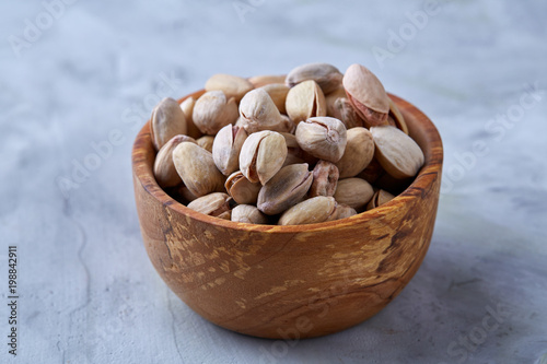Salted pistachios on a wooden plate over white background, top view, close-up, selective focus.