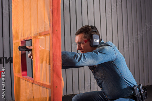 An adult man in a denim shirt shoots a gun in a shooting range through a red obstacle © Михаил Решетников