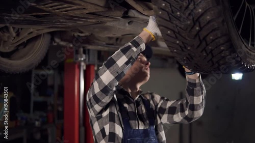 Handsome mechanic reparing a car fromthe bottom in his workshop. photo