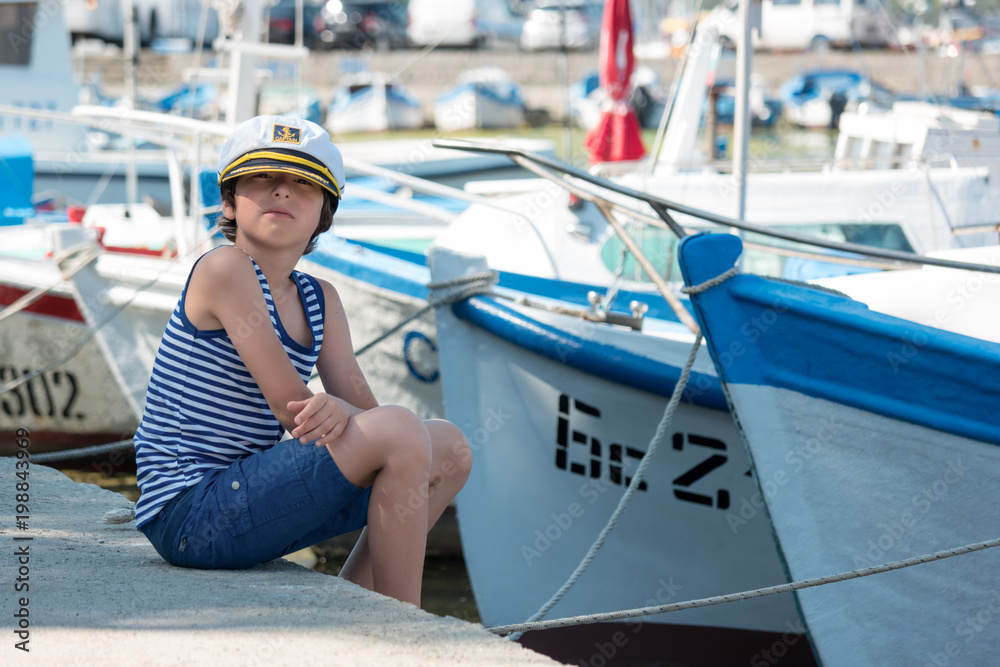 The boy is standing on the pier in the seaport.