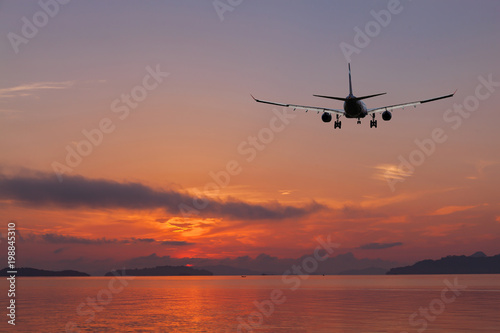 Airplane flying over tropical sea at beautiful color sunset or sunrise scenery background.