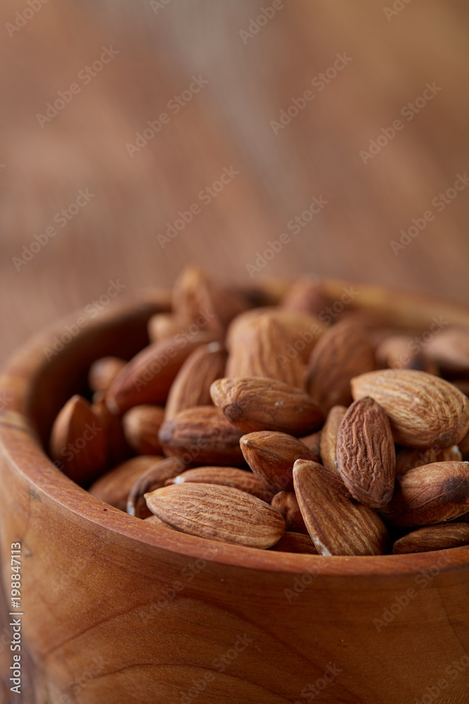 Ceramic bowl of almonds on wooden background, top view, close-up, selective focus.