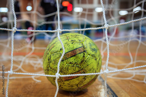 Handball ball in nets. Blurred court and athletes background. Close up view.