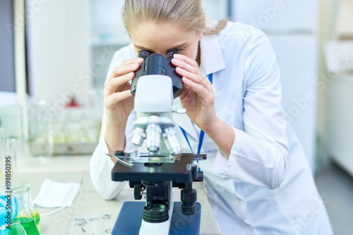 Serious experienced female scientist working with modern microscope while holding scientific research in laboratory