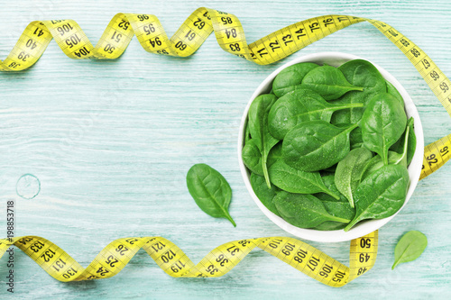 Green spinach leaves and tape measure on wooden table top view. Diet and healthy food concept.