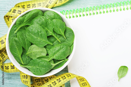 Clean notebook, green spinach leaves and tape measure on wooden table from above. Diet and healthy food concept.