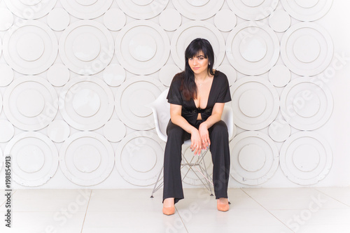 Fashion shot of a woman in black overall at soft pastel interior. Hispanic woman, body sensual and sexy 