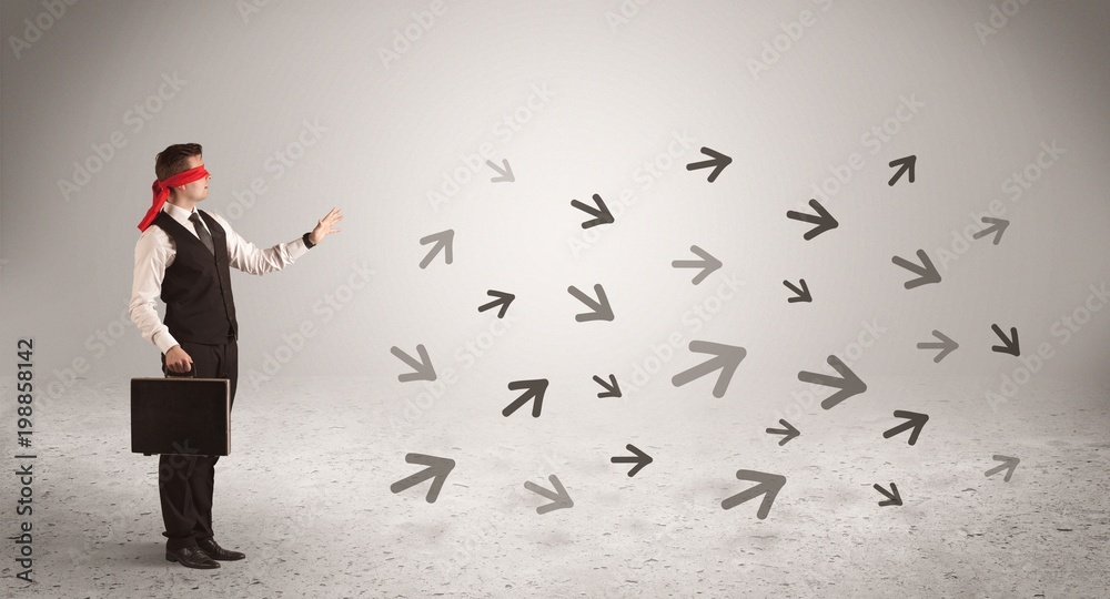 A male office worker standing blindfolded and confused with arrows pointing in different directions concept A male office worker standing blindfolded and confused with arrows pointing in different directions concept