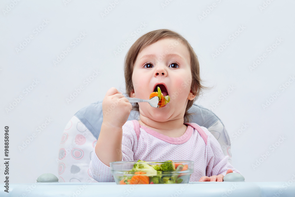 Adorable toddler girl is having fun while eating stewed vegetables on white background Adorable toddler girl is having fun while eating stewed vegetables on white background