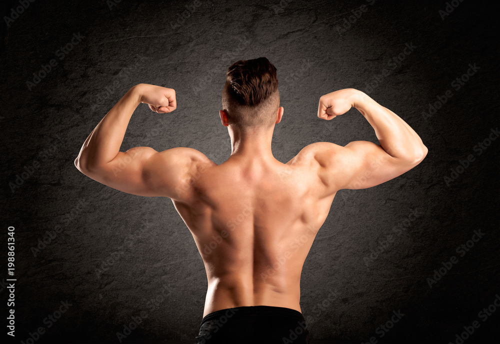 A handsome fitness guy lifting weight and showing his strong muscles in front of a black urban concrete wall concept A handsome fitness guy lifting weight and showing his strong muscles in front of a black urban concrete wall concept