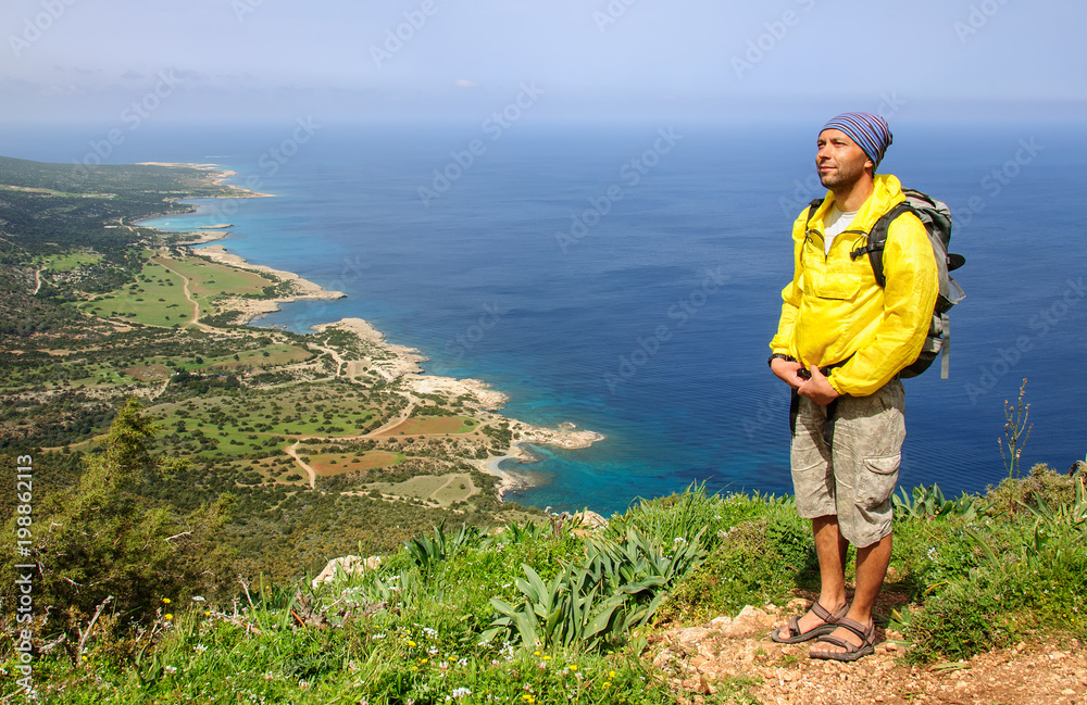 man with a backpack stands on the shore of the Mediterranean Sea and looks into the distance