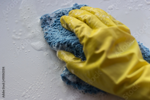 A female hand in a yellow glove washes a soapy rag surface. White background, isolated photo