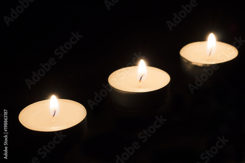 Three round burning candles on a black background.